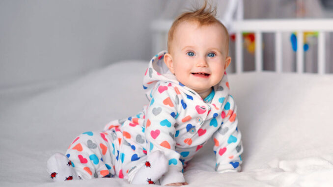 Cute smiling baby in a stylish hoodie sitting on a white blanket